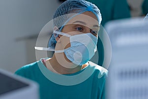 Caucasian female surgeon wearing surgical gown and face mask in operating theatre at hospital