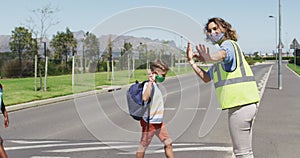 Caucasian female teacher wearing a face mask and high visibility vest stopping traffic on a pedestri