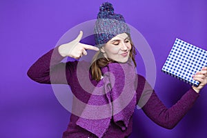 Caucasian Female Woman in Warm Knitted Hat and Violet Scarf Posing with Big Checked Wrapped Present Gift Box While Pointing