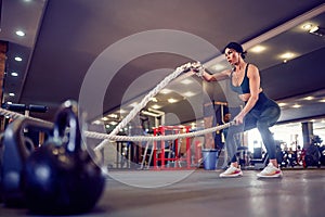 Caucasian fit woman dressed in sportsoutfit posing with battle ropes at gym