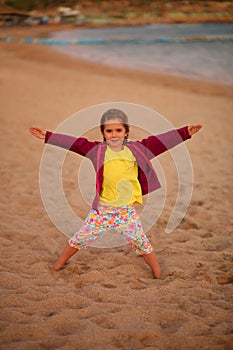 Caucasian five year old girl jumping on the sunset beach with her hands and legs widespread