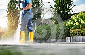 Caucasian Garden Worker Pressure Washing Residential Driveway Using Modern Pressure Washer