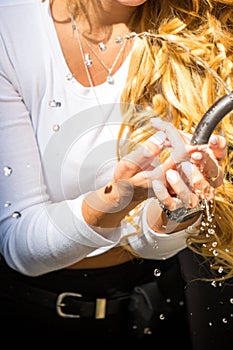 Caucasian girl with blond curly hair drinks water from a historical traditional drinking fountain outdoors in Rome. Hot