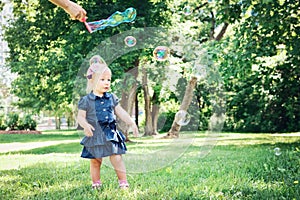 Caucasian girl child in blue dress standing in field meadow park outside, making soap bubbles