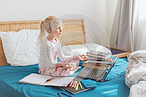 Caucasian girl child meditating in bed and learning online on laptop Internet. Virtual class lesson on video during home self
