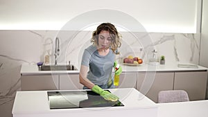 Caucasian girl cleaning cooktop cooking panel on kitchen. Young woman cleaning up the perfect surface of black ceramic