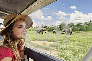 A Caucasian girl in a hat looks at animals in the savannah. The concept of travel and adventure in the wild. Young woman