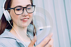 Caucasian girl in headphones smiles and listens to music while looking into a smartphone