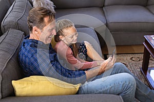 Caucasian girl and her grandfather spending time together sitting on a couch and using a phone