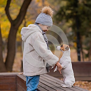 Caucasian girl holding a dog by the paws for a walk in the autumn park. Jack Russell Terrier stands on its hind legs on