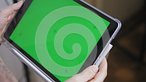 Caucasian girl holding a tablet with a green screen in her hands. Close-up of female hands with a gadget, with a chroma