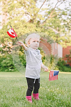 Caucasian girl holding waving American and Canadian flag in park outside celebrating 4th july