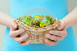 Caucasian girl holds in her hands basket with Easter painted yellow eggs. Close-up