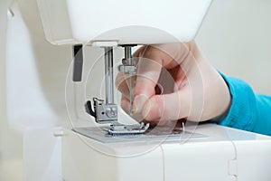 Caucasian girl inserts a thread into the needle of the sewing machine.