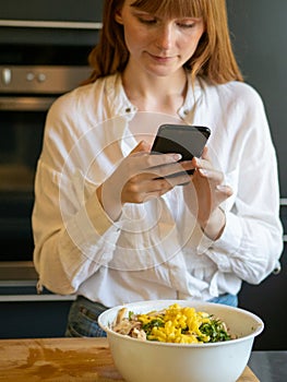 Caucasian girl in a modern kitchen, consult her cell phone to know the recipe she is going to prepare with vegetables