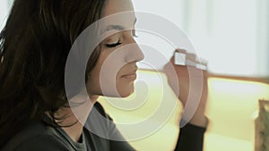 Caucasian girl with a pleasant face, sitting inside of cafe, touching her long brown hair and looking carefully down