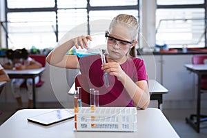 Caucasian girl pouring chemical from beaker into test tube in science class at laboratory