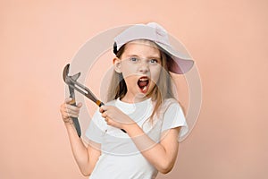 Caucasian girl of primary school age in a baseball cap with a wrench on a pink background, father's daughter tomboy
