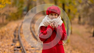 Caucasian girl in a red coat and beret walks along the railway tracks in the park in autumn.