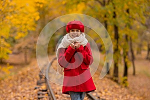 Caucasian girl in a red coat and beret walks along the railway tracks in the park in autumn.