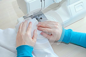 Caucasian girl sews cotton white fabric on the sewing machine