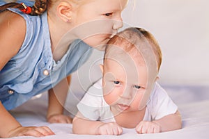 Caucasian girl sister kissing little baby, lying on bed