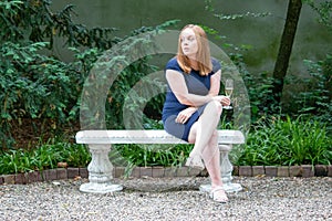 Caucasian Girl sitting on a bench and looking longingly while holding a drink