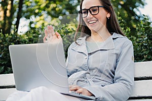 Caucasian girl sitting on a park bench and video chatting via laptop