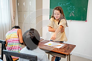 Caucasian girl stand in front of classroom and point to Asian boy look like angry with fun during learn in school