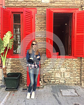 Caucasian girl in sunglasses. A girl with long hair in a denim suit and white sneakers the girl stands near an old brick house wit