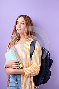 Caucasian girl teen student in casual wear with backpack and books isolated on purple background studio portrait