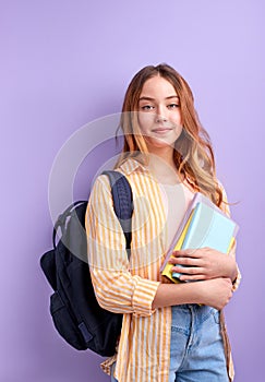 Caucasian girl teen student in casual wear with backpack and books isolated on purple background studio portrait, look