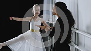 Caucasian girl teenager student ballerina in tutu doing dancing exercises near ballet barre listening to explanations