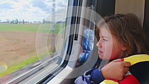 Caucasian Girl Travelling on High Speed Passenger Train Looking Through Window Eating Snacks and Hugging Plush Mascot