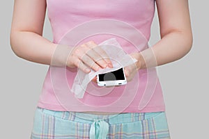 Caucasian girl wipes a white smartphone with disinfectant wipe