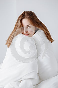 Caucasian girl woman with long red hair sitting in bed wrapped covered with blanket