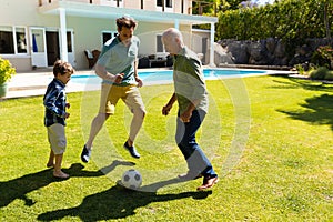 Caucasian grandfather, father and son playing football together in the garden