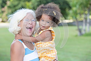 Caucasian grandma carrying her hispanic granddaughter