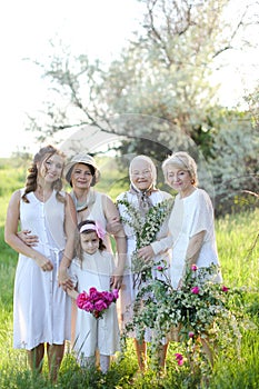 Caucasian grandmother in white dress with daughters and granddaughters outside.