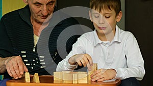 Caucasian grandpa with grandson build together towers from wooden cubes. A boy and his grandfather are playing board games, buildi