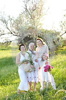 Caucasian granny in white dress with daughter and granddaughters outdoors.
