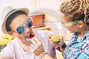 Caucasian guy and adult woman at home in the terrace having breakfast together with a funny face of the teenager whil he`s eating