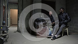 Caucasian guy and black guy are hidin in a basement during a war