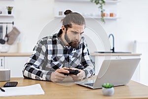 Caucasian guy in checkered shirt using remote console for playing video games.