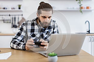 Caucasian guy in checkered shirt using remote console for playing video games.