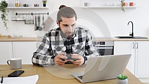 Caucasian guy in checkered shirt using remote console for playing video games.
