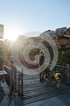 Caucasian guy with dreadlocks stands on a pedestrian bridge in the center of the old town Tbilisi with two dogs and
