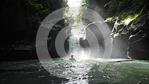 Caucasian guy jumps and swim in the tropical rainforest waterfall at summer day.