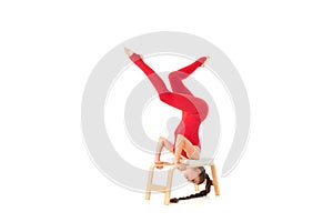 Caucasian gymnast with athletic body stands on her head, does warm-up and stretch muscles