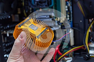 Caucasian hand holding orange plated computer heatsink and pc internals in blurry background